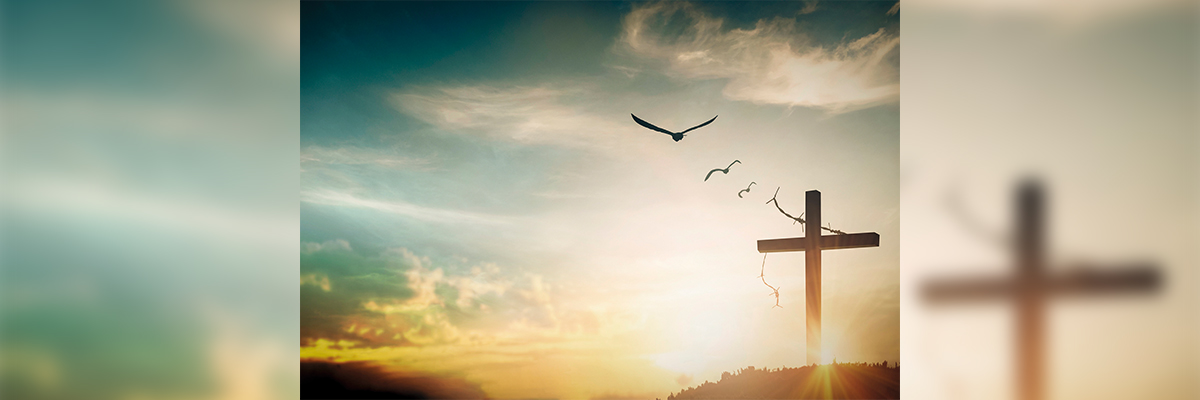 Imagen de una cruz iluminada con aves en vuelo al amanecer