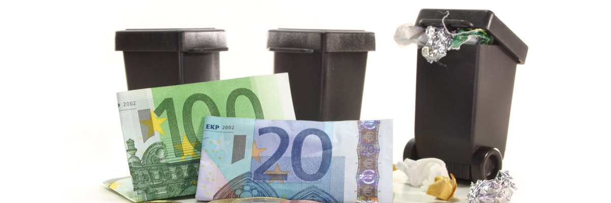 Tres contenedores de basura en miniatura con billetes de euro (100 y 20) frente a ellos sobre superficie blanca