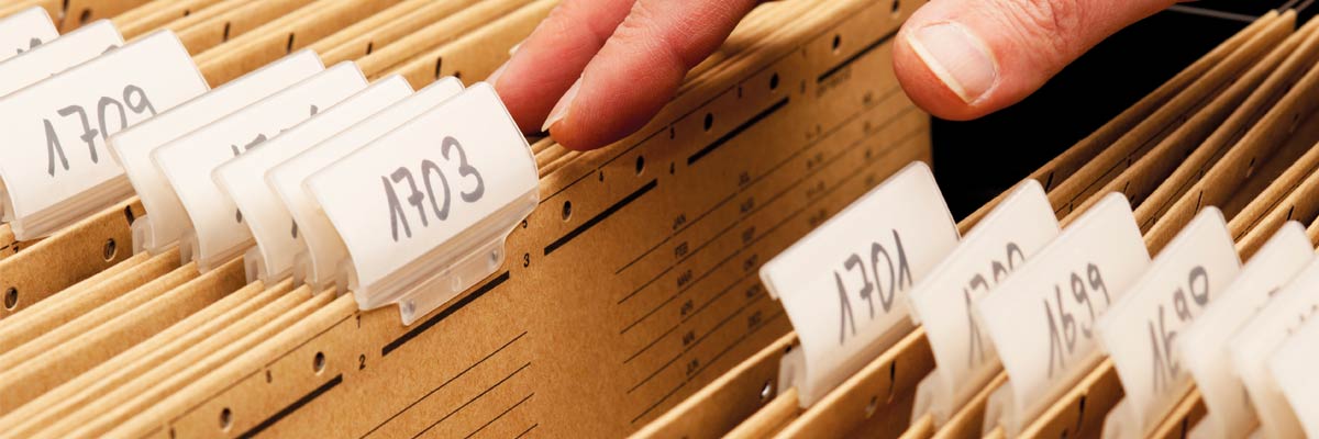 Mano revisando fichas de archivo numeradas en cajón de expedientes, gestión documental y organización administrativa.