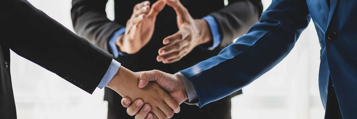 Dos personas estrechan la mano frente a un tercero que aplaude, simbolizando acuerdo amistoso.