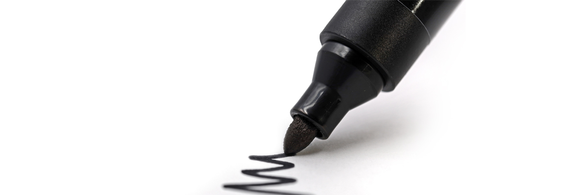 Punta de rotulador negro trazando una línea zigzagueante sobre papel blanco