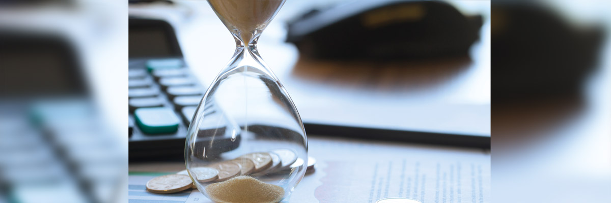 Reloj de arena con arena cayendo sobre monedas, calculadora y documentos difuminados al fondo