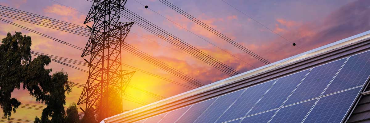 Paneles solares junto a torres eléctricas al atardecer: integración de renovables y red de distribución energética.