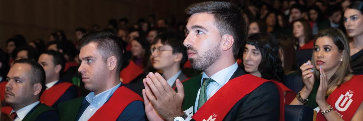 Estudiantes con toga y banda aplauden en el auditorio durante la ceremonia de graduación