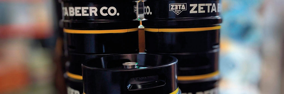 Barriles negros de cerveza ZETA apilados con logotipo blanco y franja amarilla en almacén cervecero.