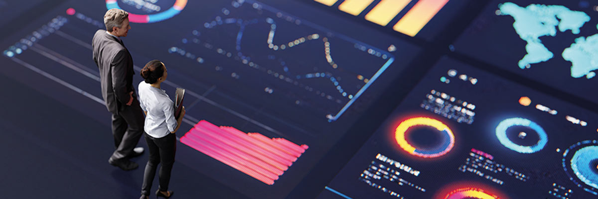 Personas observan pantalla digital con gráficos, mapas y datos en entorno de análisis empresarial.