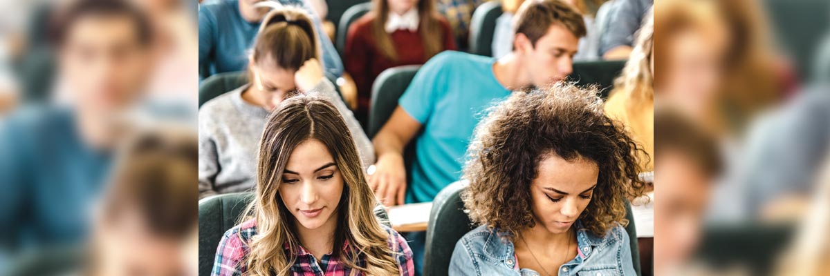 Estudiantes en un aula universitaria sentados en fila, concentrados en sus apuntes
