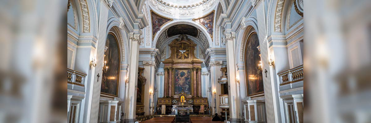 Interior del Real Monasterio de la Encarnación de Madrid, columnas blancas, altares dorados y bancos de madera, luz entrando por la cúpula