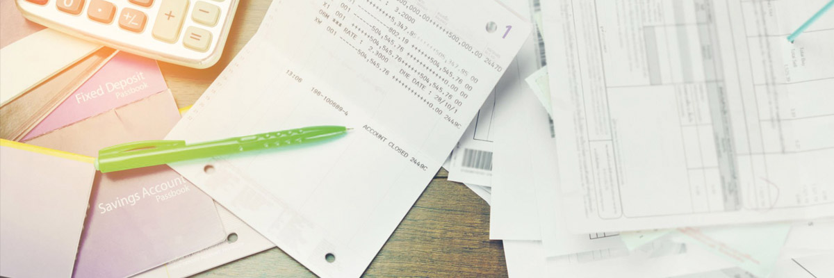 Documentos y extractos bancarios sobre mesa, un bolígrafo verde y libreta de cuentas junto a calculadora