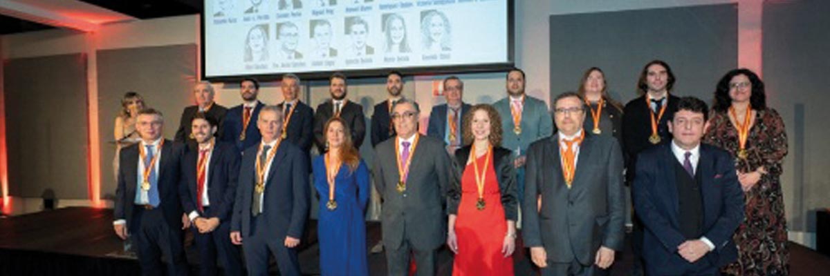 Grupo de personas con medallas posando en un evento formal con una pantalla de fotos detrás