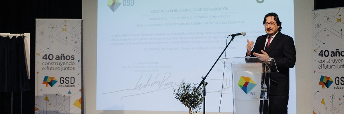 Persona en traje dando un discurso junto a un podio con logotipo GSD y una pancarta “40 años construyendo el futuro