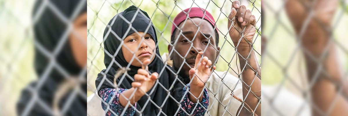 Hombre y niña migrantes tras una valla
