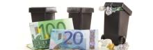 Tres contenedores de basura en miniatura con billetes de euro (100 y 20) frente a ellos sobre superficie blanca