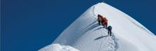 Grupo de escaladores ascendiendo una empinada cumbre nevada bajo un cielo azul claro, simbolizando determinación y trabajo en equipo en el montañismo