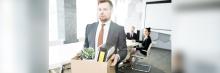 Empleado sale de la oficina con caja de pertenencias tras un despido; imagen sobre despido y transición laboral.
