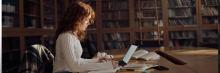 Estudiante universitaria estudia en biblioteca con portátil y apuntes, concentración y estudio académico.