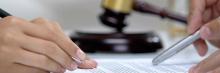 Manos firmando documento junto a mazo de juez, símbolo de sentencias, consultas y novedades en materia tributaria.