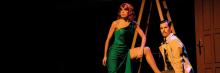 Escena de 'Los 39 escalones' en Teatro Flumen: actriz con vestido verde y actor en persecución cómica