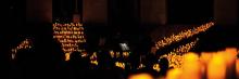 Sala oscura iluminada por cientos de velas dispuestas en escaleras, músicos tocando en penumbra