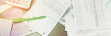Documentos y extractos bancarios sobre mesa, un bolígrafo verde y libreta de cuentas junto a calculadora