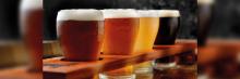 Cuatro vasos de cerveza artesanal de distintos colores colocados en una parrilla de madera para degustación