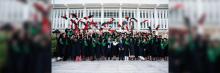 Numerosos graduados en toga y birrete frente a edificio blanco, lanzan sus birretes al aire festejando.