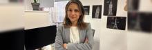 Mujer con blazer gris y brazos cruzados en una oficina