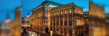 Fachada iluminada de la Ópera Estatal de Viena al anochecer, con tráfico y luces de ciudad alrededor